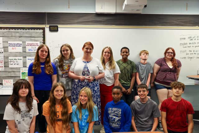 This is a group of people posing for a picture in front of a classroom chalkboard.